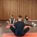 A group of adults practicing yoga and stretching on mats in a wooden panelled room.