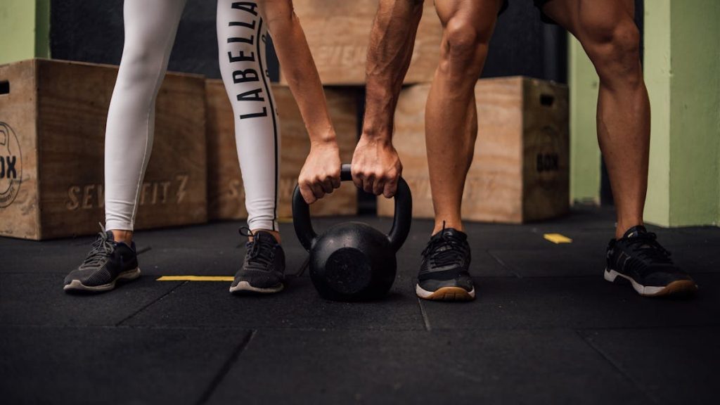 A man and woman engaging in CrossFit training with a kettlebell at an indoor gym in Brazil.