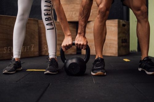 A man and woman engaging in CrossFit training with a kettlebell at an indoor gym in Brazil.